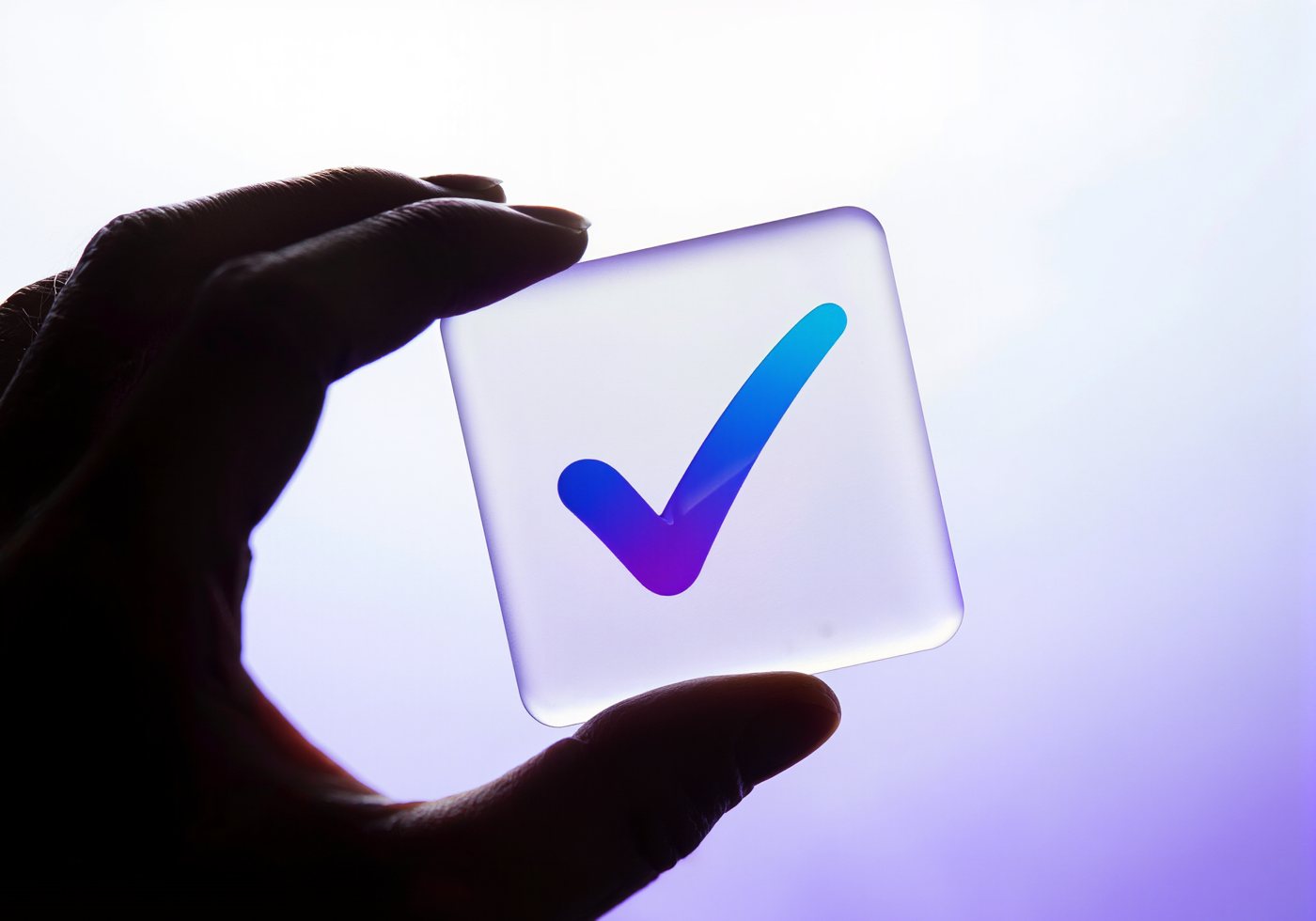 A hand holding a glass tile with a tick mark